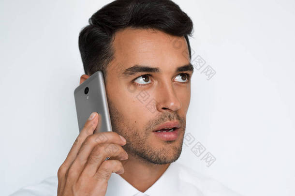 美丽的特写照片的年轻人使用手机灰色<strong>背景</strong>。商人用他的智能手机<strong>讲话</strong>。裁剪面.