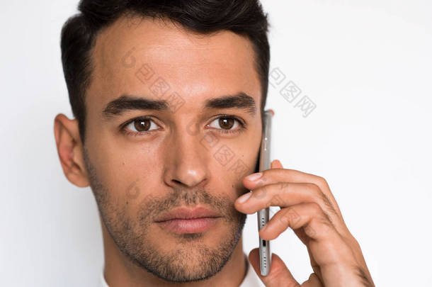 用手机合上英俊的年轻男士的肖像, 看着集中的一面。浅灰色背景下智能手机销售有吸引力的商人.
