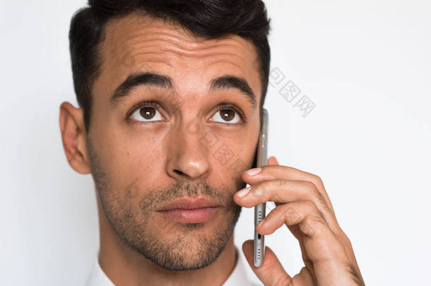特写肖像的年轻英俊男子使用手机灰色背景。商人用他的智能手机讲话。<strong>查找</strong>.