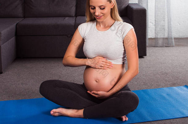 两个<strong>瑜伽</strong>。美丽的年轻孕妇看着她的肚子微笑, 而坐在<strong>瑜伽垫</strong>在家里的内部