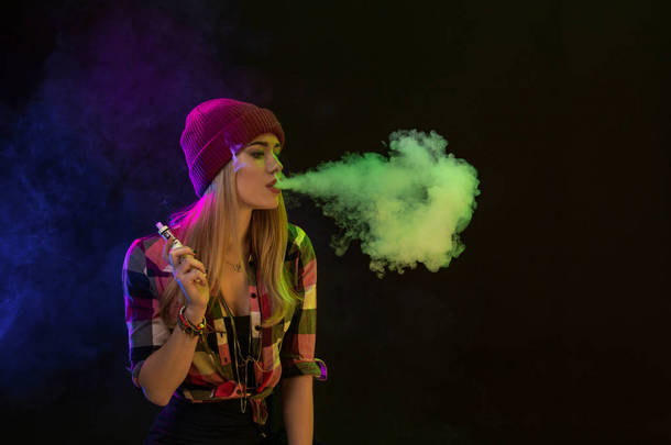 Vaping 女孩年轻的时髦女人 vape 在黑色背景上的电子香烟。嘻哈风格。工作室拍摄
