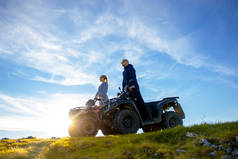 美丽的情侣看着夕阳从山上坐在亚视 quadbike