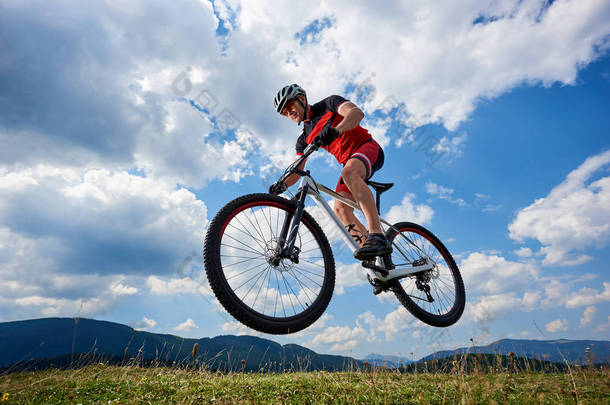 运动运动员骑自行车在专业运动衫和头盔跳跃骑脚踏车与天空和遥远的山在背景下, 户外极限运动概念
