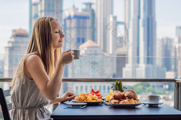 一个年轻的女人正在<strong>阳台</strong>上吃早饭。早餐桌与咖啡果子和面包 croisant 在<strong>阳台</strong>反对大都市的背景