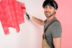 微笑的人在工作整体和头带涂在红色油漆辊墙
