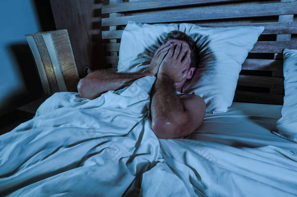 年轻的悲伤和绝望的男人躺在床上哭泣压抑的脸与手遭受抑郁症和压力看起来沮丧与一些问题在悲伤和生活方式的概念