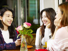 三愉快的美丽的年轻亚洲妇女坐在桌边聊天在咖啡馆或茶馆里谈话.