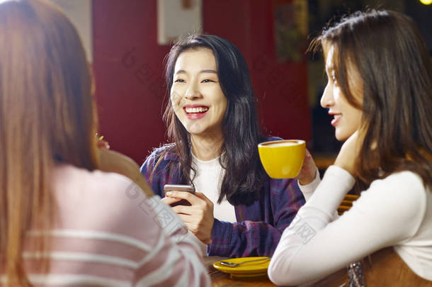 三愉快的美丽的年轻亚洲妇女坐在桌边聊天在咖啡馆或茶馆里谈话.