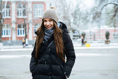 长发美丽的女孩穿着暖和的羽绒服穿过城市的街道, 在冬天, 微笑着