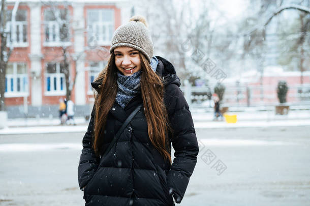 长发美丽的女孩穿着暖和的<strong>羽绒服</strong>穿过城市的街道, 在冬天, 微笑着