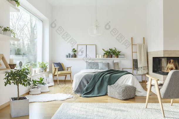 灰色扶手椅和图案<strong>脚凳</strong>在宽敞的 scandi 卧室内饰的绿色毯子床旁边