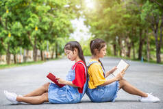 漂亮的亚洲双胞胎女孩或学生在公共公园看书。使用的教育概念