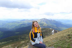 身穿黄色夹克的年轻漂亮女性游客坐在大山上.