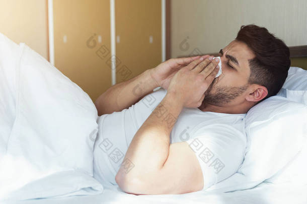 年轻人打喷嚏和覆盖鼻子与组织躺在床上