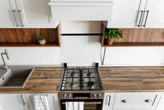 时尚的浅灰色厨房内饰与现代橱柜和不锈钢家电在新家。斯堪的纳维亚风格的设计。绿色植物装饰, 木台面, 水槽和火炉