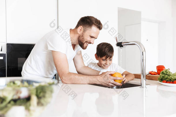 照片的开朗的年轻人<strong>爸爸爸爸</strong>做饭与他的儿子在家中的厨房.