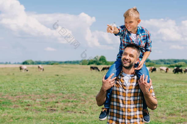 快乐的父亲带着微笑的儿子在脖子上, 看着<strong>远离</strong>田野