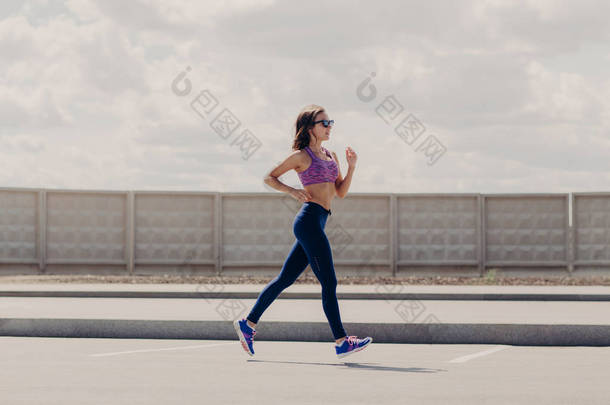 户外拍摄的运动女性慢跑与苗条的身体运行在路上, 准备跑马拉松, 穿紫色的顶部, leegings 和运动鞋, 感觉坚定。健康生活方式与体育理念