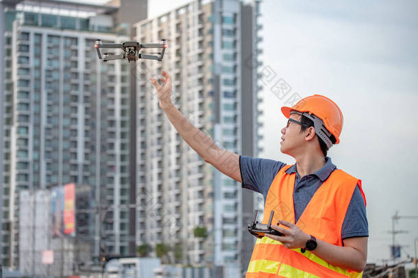 年轻的亚洲工程师驾驶飞机在建筑工地上空飞行。用无人飞行器 (无人机) 进行土建工程现场勘察.