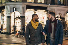 在冬天, 两个人走在城市街道上的前景色。两个男人都穿着暖和的衣服, 看着对方说话。.