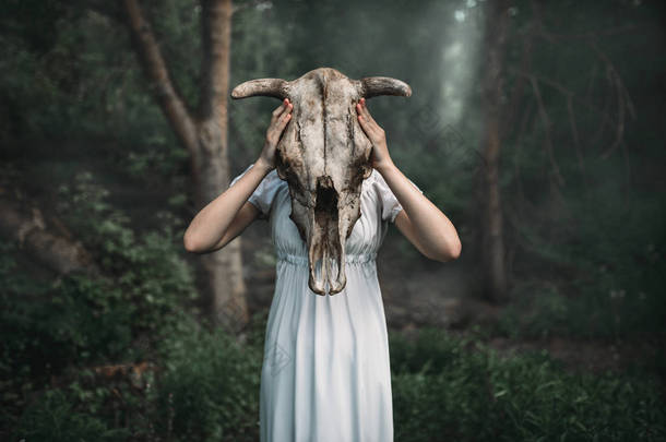 <strong>女性</strong>受害者在白色礼服与头骨的动物而不是头, 森林在背景。照片中的恐怖风格, 驱魔