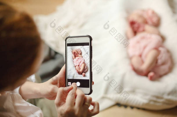 妈妈把她的新生女儿裹在一条柔软的粉红色毯子里, 头上戴着粉红色的头巾, 头顶上有一朵花和一顶戴着白色针织毯子的皇冠。选择性聚焦