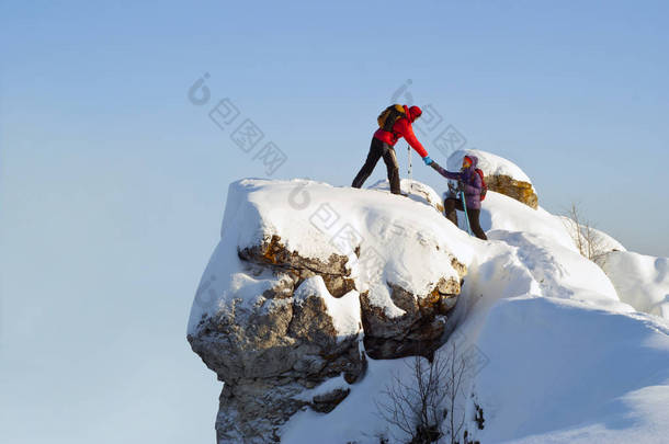 两个徒步旅行者在山顶上过冬;一个男人帮助一个女人爬上一只<strong>纯粹</strong>的石头