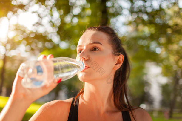 夏季公园锻炼后, 年轻的运动妇女喝水。健康的生活方式。积极的生活方式