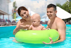 快乐的父母与小婴孩在游泳池在阳光明媚的天, 室外