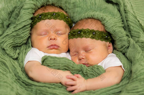 两个<strong>相同</strong>的双胞胎婴儿女孩身穿绿色头巾依偎在一起的毯子牵手