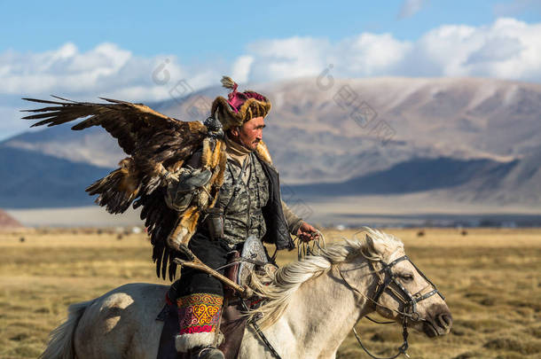 Sagsay, 蒙古-2017年9月28日: 金黄老鹰猎人, 当狩猎对野兔在他的胳膊拿着一只金黄老鹰在西部蒙古的沙漠山.