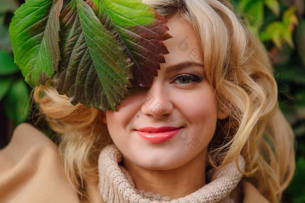 年轻美丽的妇女穿着<strong>毛衣</strong>和<strong>大衣</strong>站在野生葡萄的背景下, 在秋季公园的叶子接近的脸