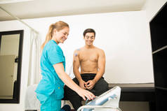 微笑的男性运动员在诊所获得理疗师的电疗法
