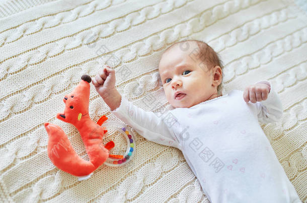 新生女婴躺在针织毯上, 微笑着看着五颜六色的木制拨浪鼓玩具。1月大的孩子在家