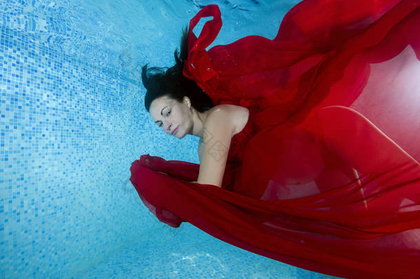 穿着红色连衣裙的孕妇在水池水下潜水