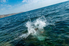 一个男孩正从悬崖上跳到海里, 在炎热的夏日里溅起了大水花。海滩上的假日。积极旅游与休闲的概念