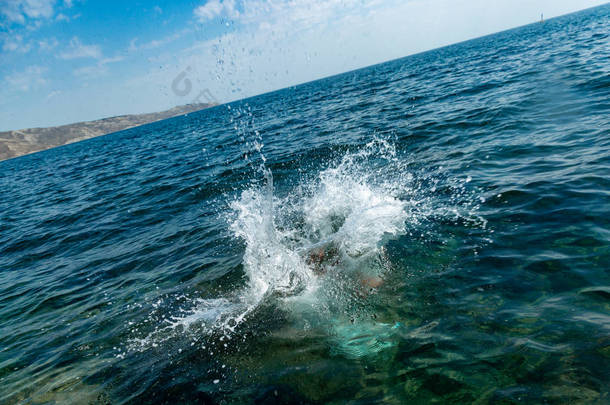 一个男孩正从悬崖上跳到海里, 在炎热的<strong>夏日</strong>里溅起了大水花。海滩上的假日。积极<strong><strong>旅</strong>游</strong>与休闲的概念