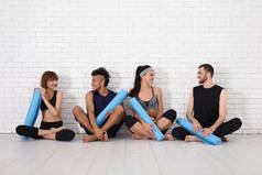 小组运动的人与瑜伽垫坐在附近白色砖墙