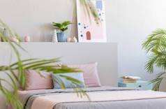 明亮的卧室室内装饰的真实照片, 带有粉彩床单的双层床, 床头桌上的书籍和现代艺术绘画