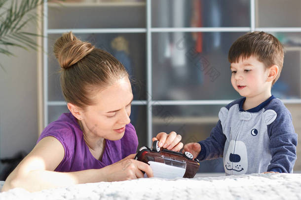 欧洲深情的妈妈试着修理玩具车, 和她的儿子一起度过闲暇时光, 照顾自己, 努力在未来培养真正的男人, 在家里舒适的房间里摆姿势。小男孩玩妈妈和玩具