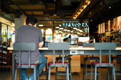 坐在高椅子上的无名男子的肖像和他的笔记本电脑在咖啡店工作。共同工作空间概念