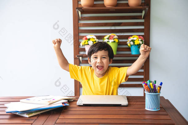 儿童作业。年轻的混血男孩完成他的家庭作业关闭笔记本电脑, 开始欢呼。心情很愉快。返回学校概念.