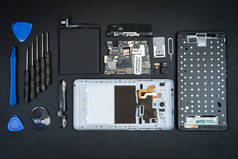 拆卸的手机与被删除的屏幕和特殊用途工具在黑色桌面上。智能手机的详细信息。电话修理工工作场所