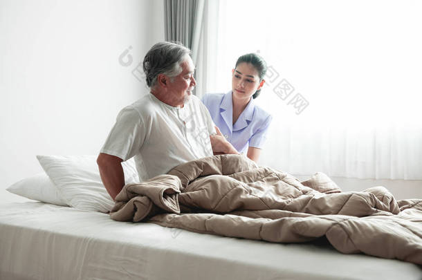 老人在床上试图起床和护士帮助他。老亚裔男子和美丽的亚洲护士妇女在卧室和开放窗帘。高级家庭<strong>服务理念</strong>.