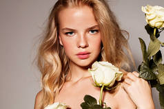 美丽的年轻模特与白玫瑰。完美的焕发肌肤。金发。清新的外观.