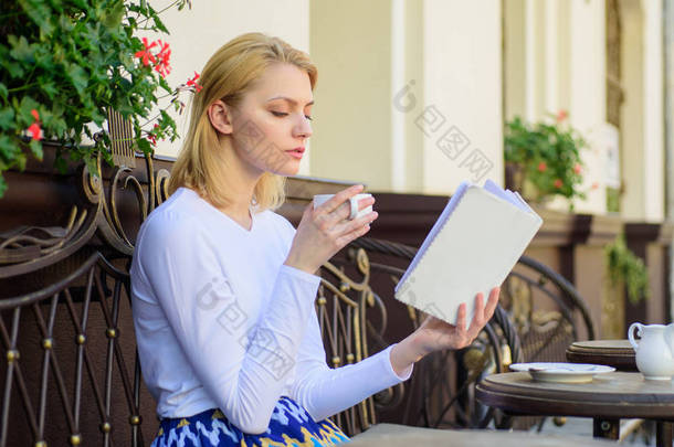 女孩喝咖啡, 而阅读新畅销书的流行作家。完美的早晨概念。杯咖啡和有趣的书最佳组合完美的周末。妇女有饮料咖啡馆露台室外