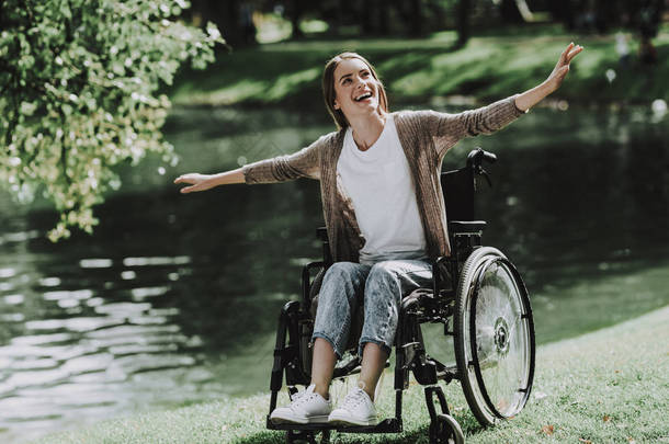 在湖边的公园里坐轮椅的年轻微笑的女孩。残疾的年轻女子。在夏季公园放松身心。夏季公园的乐趣。恢复和医疗保健概念。坐着的女人。湖公园.