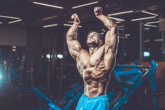 英俊的年轻适合肌肉的白种人的模型外观锻炼训练在健身房获得重量抽肌肉, 姿势, 饮料水健身和健美运动营养概念