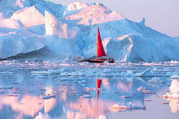 在极地夏季的午夜太阳季节, 小<strong>红帆船</strong>在迪斯科湾冰川的漂浮冰山之间游弋。伊卢利萨特, 格陵兰.