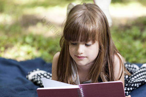 小可爱的女孩躺在草地上, 看书欣赏躺在草地上的自然小女孩, 仔细阅读这本书